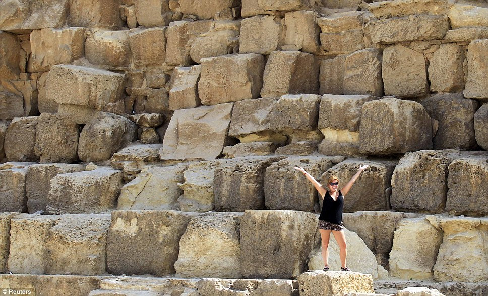 A tourist gestures as a friend takes a picture for her on the huge steps that make up the biggest pyramid in Giza