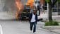 A man walks past a burning police vehicle, during unrest