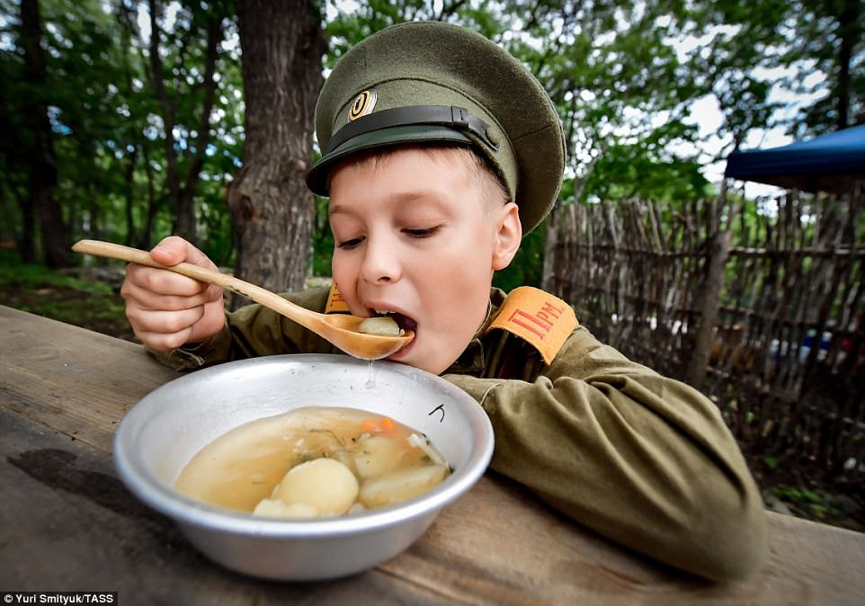 The park also includes a variety of historical reenactments, showing different periods of Russian military history. In this image, a boy eats at a soup kitchen