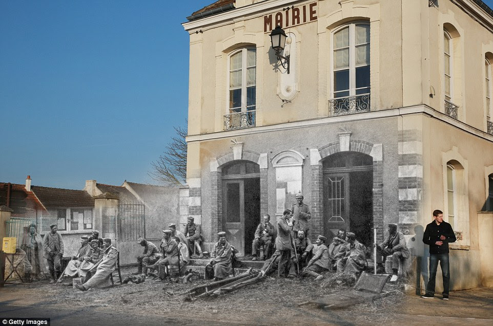 Relaxation: German troops are sit outside the Varreddes town hall in northern-central France in 1914. In the present day, a man in jeans stands next to the wall