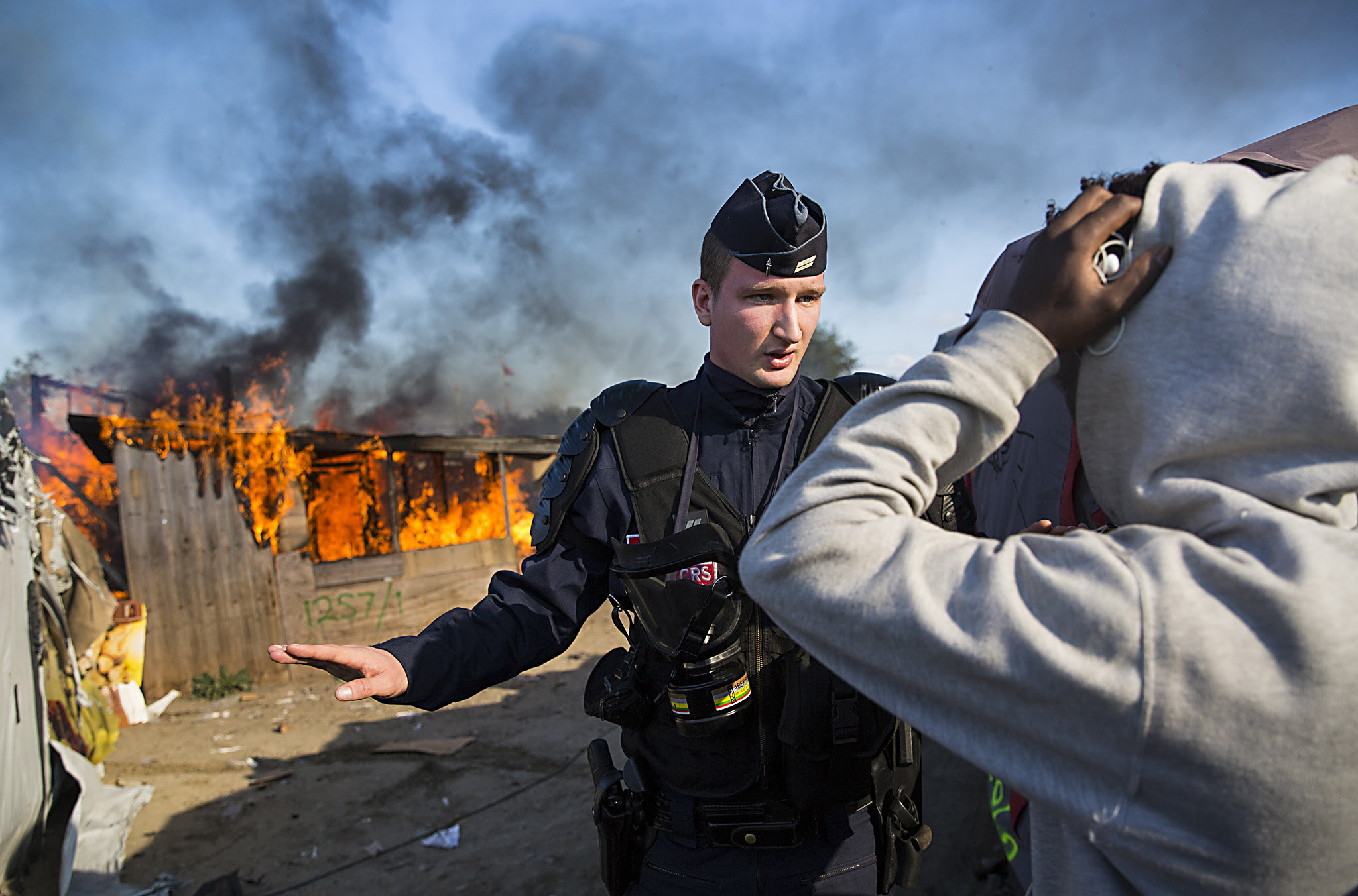 A police officer stands guard after migrants burn down a shelter as authorities move in to clear the Jungle migrant camp on October 25, 2016 in Calais, France. Migrants are leaving the Jungle migrant and refugee camp by coach for a second day as French authorities clear the camp of an estimated 7000 people ahead of its demolition. (Photo by Jack Taylor/Getty Images)