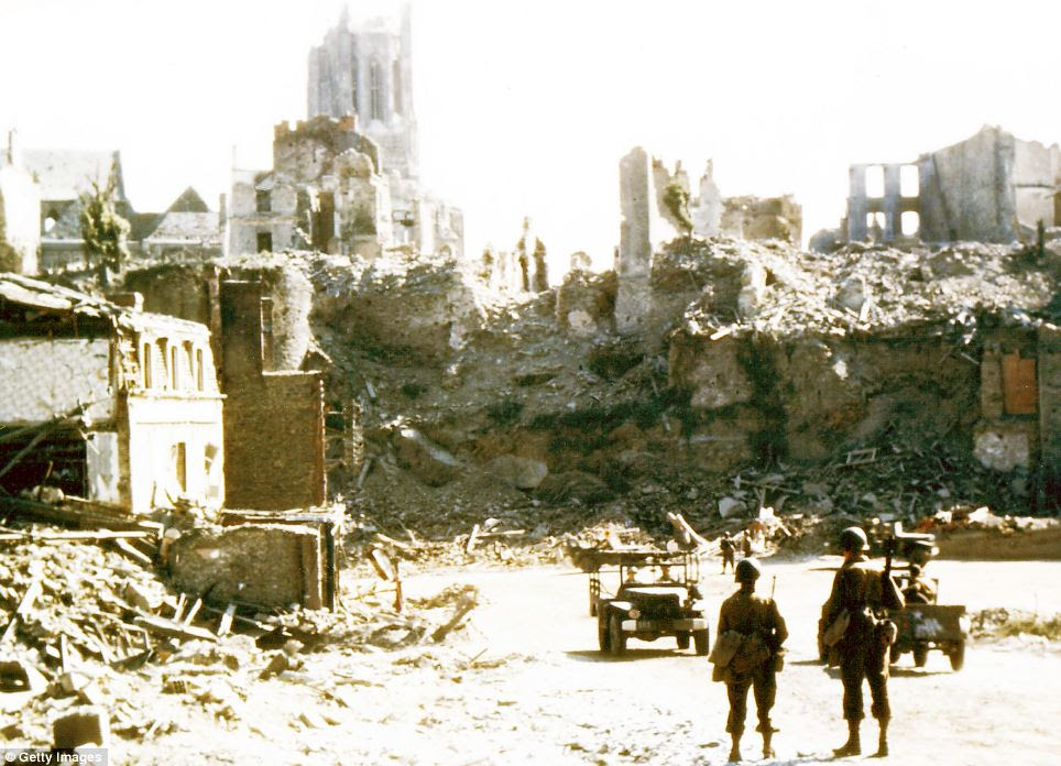 American soldiers watch U.S. Army jeeps drive through the ruins of Saint-Lo, the town was almost totally destroyed by 2,000 Allied bombers when they attacked German troops stationed there during Operation Overlord in June 1944