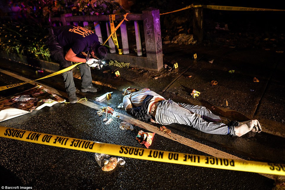 A police investigator takes pictures of the corpse of a suspected drug pusher and victim of a vigilante-style execution with his hands tied and head wrapped with tape on a street in Manila