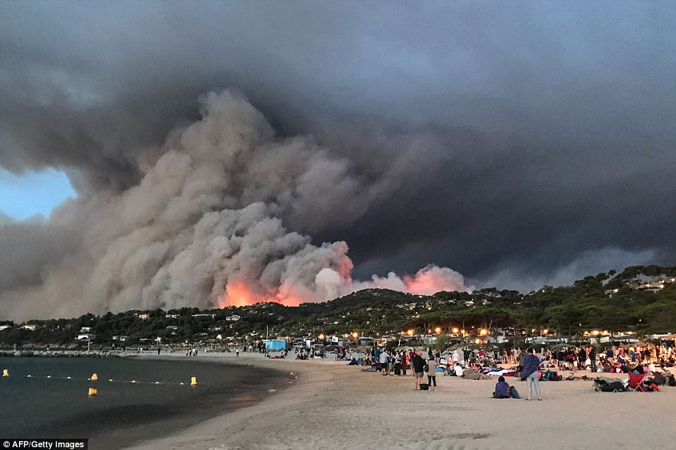 Evacuated people found refuge on the beach and look at a fire burning the forest in Bormes-les-Mimosas, at sunrise on July 26, 2017