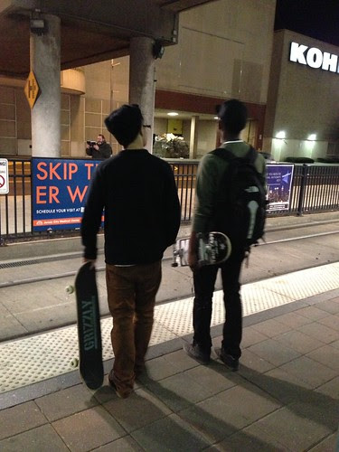 Two skateboardres, watching the light rail preacher