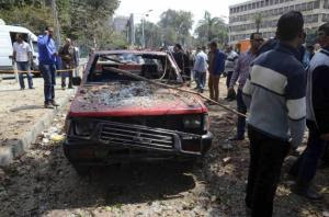 People stand near a damaged car after explosions near Cairo University