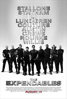 Nine armed men dressed in black standing shoulder to shoulder, Sylvester Stallone front and center.