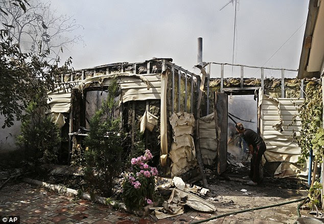 A woman inspects the damage done to her home in the shelling, as she puts out the last of the flames