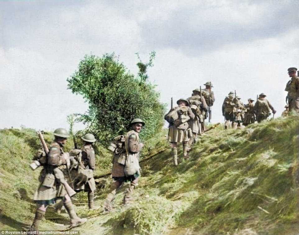 Scottish troops march with combat gear and rifles slung over their backs as they make their way over a grassy mound during the Battle of the Canal du Nord, 1918