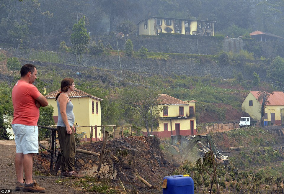 Um casal olhar para as casas evisceradas nos arredores de Funchal, capital da Ilha da Madeira, em Portugal. Mais de 1.000 turistas foram evacuados como incêndios ameaçam resorts na ilha