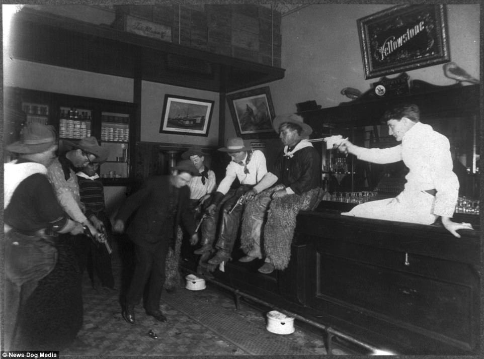 Dance! Seven men in an unknown saloon, possibly in Wyoming, shoot down at the floor, forcing another man to jump and 'dance' to avoid the bullets. While the cowboys have all their revolvers pointed at the man's feet, the bartender is aiming his semi-automatic German Mauser straight at the unlucky bar-goers head. 