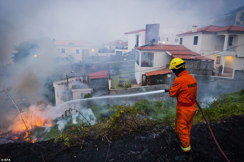 Um bombeiro Português mangueiras para baixo chamas em uma área residencial da cidade de Funchal, na Madeira. Três pessoas são relatados para ter sido morto