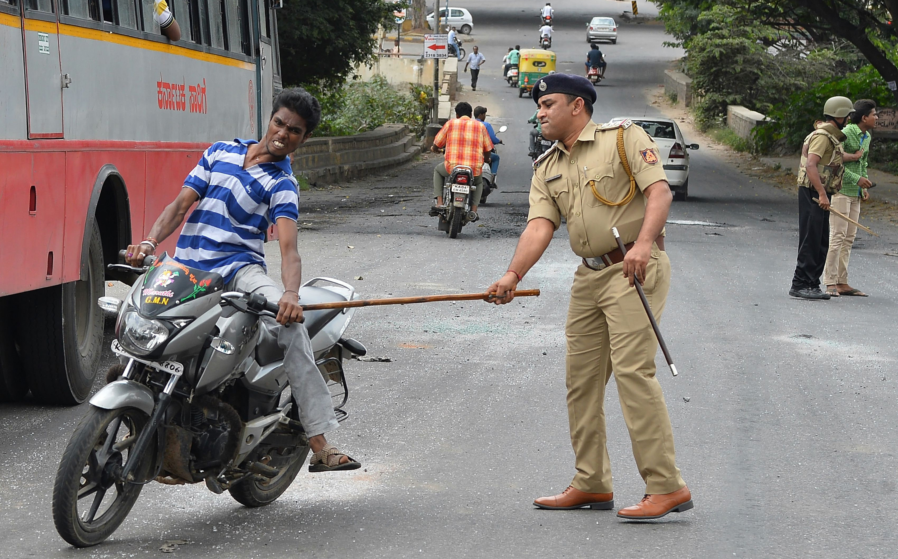 A police personnel canes a motorcyclist during a curfew following violence in the city due to the Cauvery water sharing dispute with neighbouring state Tamil Nadu, in Bangalore