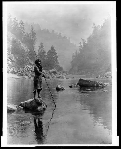 Description of  Title: A smoky day at the Sugar Bowl--Hupa.  <br />Date Created/Published: c1923 June 30.  <br />Summary: Hupa man with spear, standing on rock midstream, in background, fog partially obscures trees on mountainsides.  <br />Photograph by Edward S. Curtis, Curtis (Edward S.) Collection, Library of Congress Prints and Photographs Division Washington, D.C.