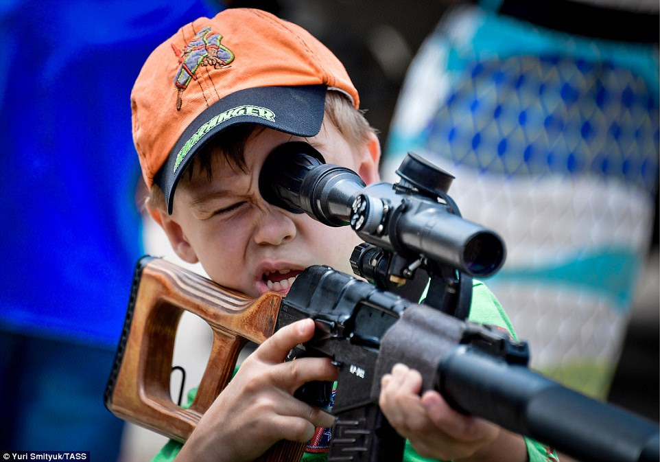 A young boy grimaces as he gazes through the viewer of a rifle with a wooden handle, one of the many exhibits at the event