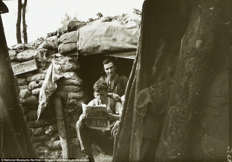 Reading the newspaper: Soldiers in the summer of 1916 at Ploegsteert Wood near Messines in Belgium. A 'keep down' sign can be seen left