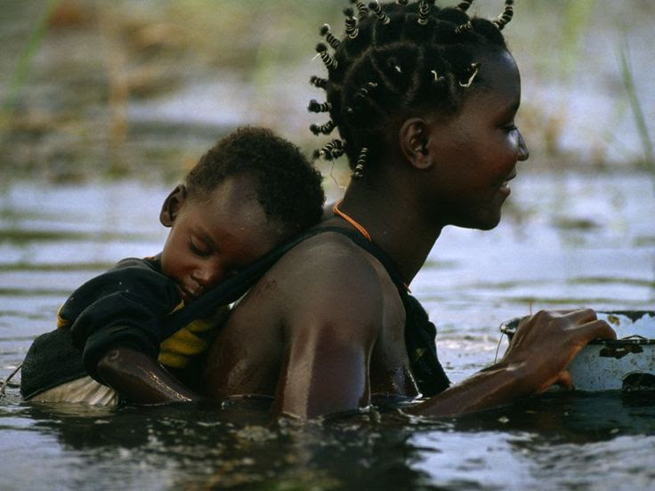 Africa | Sights and Sounds. Mbukushu mother and child crossing the flooded Okavango River in Botswana