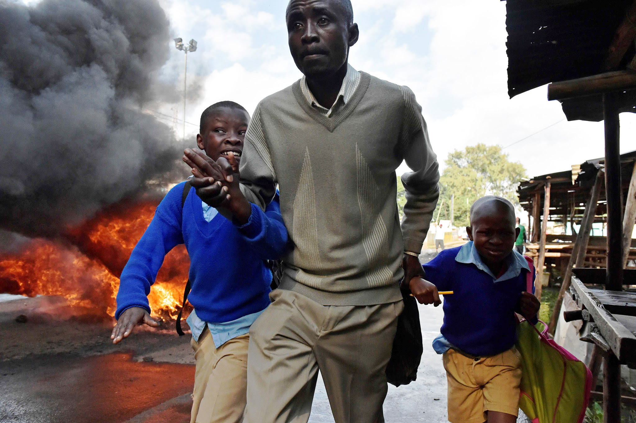 TOPSHOT - A man leads school children away from teargas and a burning barricade in Kibera slum, Nairobi on May 23, 2016 during a demonstration of opposition supporters demanding a change of leadership at the electoral commission ahead of a vote due next year. Local media reported at least one killed in Kisumu in the west of the country, while police in Nairobi and the second city of Mombasa fought running battles with small groups of protesters. There was no immediate police confirmation of the reported death. Police had banned the planned demonstrations and scores of officers in riot gear guarded the building that houses the election commission headquarters in the centre of the capital. / AFP PHOTO / CARL DE SOUZACARL DE SOUZA/AFP/Getty Images