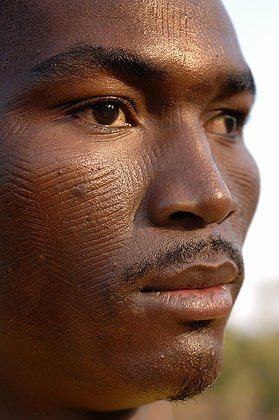 Africa | A man shows the scarifications on his face. Scarification is used as a form of initiation into adulthood, beauty and a sign of a village, tribe, and clan. Natitingou, Benin | © Jean-Michel Clajot