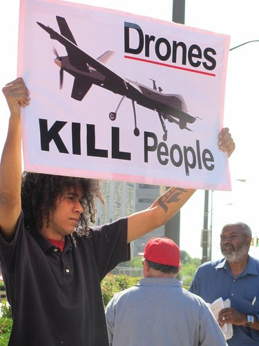 Abayomi Azikiwe in background as Jeremy holds sign at demonstration in solidarity with the people of Syria on June 27, 2012 in downtown Detroit. Demonstrations are taking place across the country in opposition to US war threats against Syria. by Pan-African News Wire File Photos