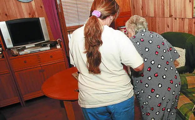 Una auxiliar ayuda a una anciana a levantarse del sofá en su domicilio. En Gipuzkoa, 4.600 personas, en su mayoría dependientes, reciben apoyo público en sus casas./JAVIER MARTÍN