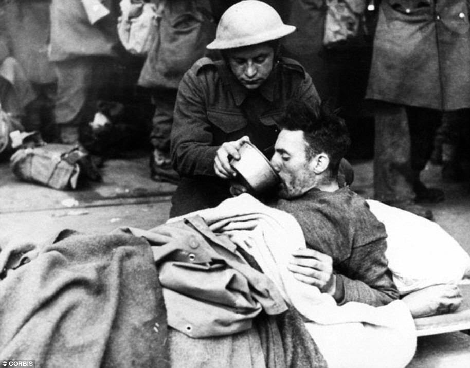 A British soldier helps a wounded man drink while waiting to be evacuated from Dunkirk in 1940
