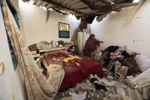 A Palestinian woman collects her belongings from a damaged bedroom after an Israeli air strike in Gaza