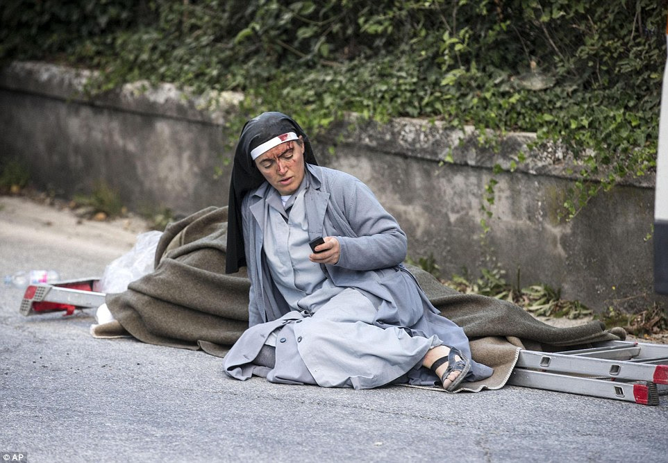 Sangrando: Uma freira ferido verifica seu telefone celular enquanto se encontra perto de uma escada e um cobertor após um terremoto em Amatrice