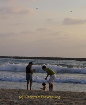 The Tel Aviv beach and life pretending to go on as normal, as helicopters fly overhead