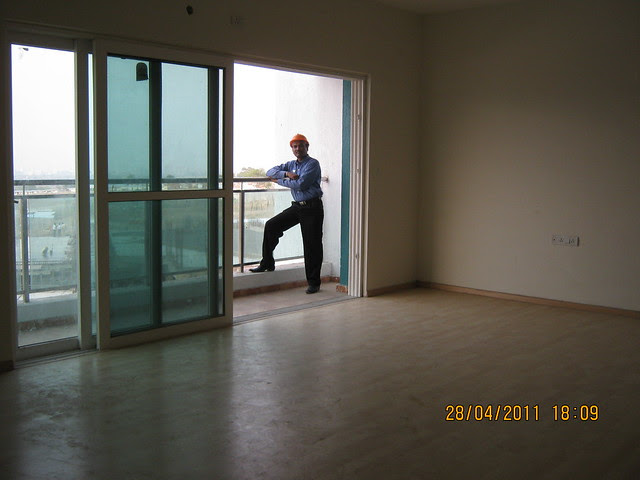 Spacious living with wooden flooring, sliding doors of the balcony with a glass railings in a flat in Sangria Towers at Megapolis Hinjewadi Phase 3, Pune