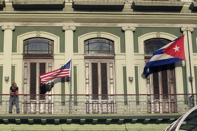 A man stands near the national flags of the U.S. and Cuba (R) on the balcony of a hotel being used by the first U.S. congressional delegation to Cuba since the change of policy announced by U.S. President Barack Obama on December 17, in Havana, January 19, 2015. The United States will urge Cuba to lift travel restrictions on U.S. diplomats and agree to establish U.S. and Cuban embassies in historic talks in Havana this week aimed at restoring relations, a senior State Department official said on Monday. REUTERS/Stringer (CUBA - Tags: POLITICS) - RTR4M2H1