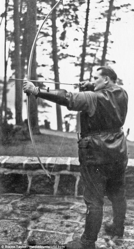 Accomplished archer Goering draws back his bow in aim, wearing protective leather gloves and forearm gauntlets, plus an all-leather outfit from top to bottom
