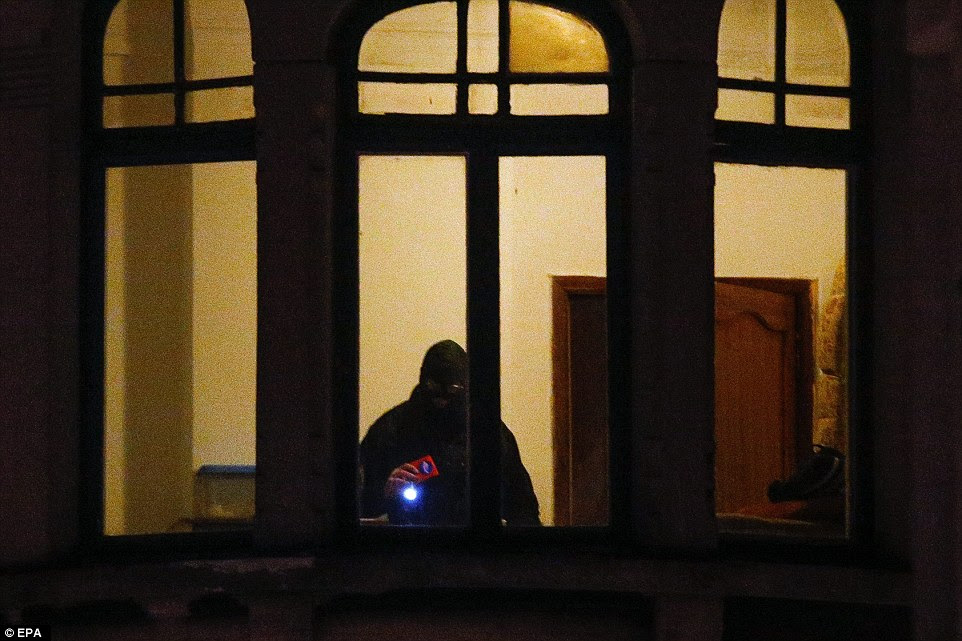 Anti-terror raids: A Belgian police officer is seen searching an apartment in the Schaerbeek area of Brussels this evening after the attacks