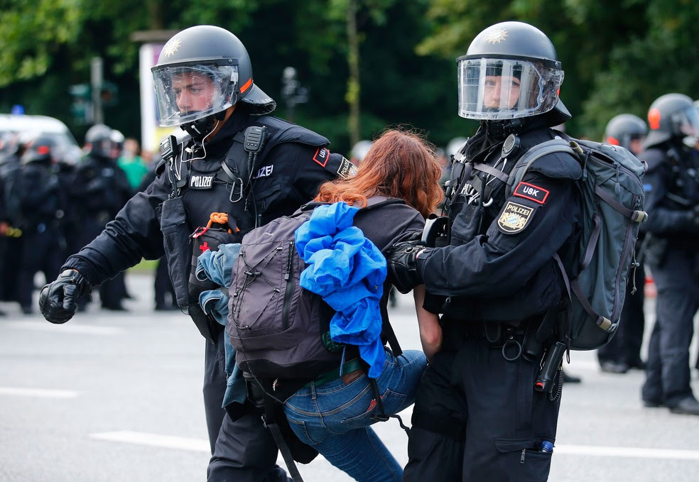 Policial retira manifestante que bloqueava rua em Hamburgo, na Alemanha, nesta sexta-feira (7)  (Foto: Hannibal Hanschke/ Reuters)