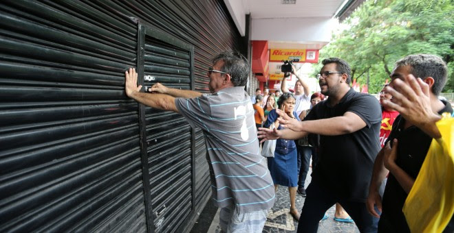 Un hombre intenta romper la puerta de una tienda durante una protesta en la huelga general de este viernes en Brasil REUTERS / Paulo Whitaker