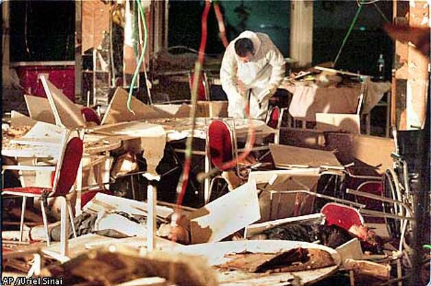 The body of a man, foreground, victim of a bomb blast, and an investigator are seen amidst the debris in the dining room of a hotel in the coastal city of Netanya, north-western Israel Wednesday March 27, 2002. A suicide bomber blew himself up Wednesday in a hotel dining room in this Israeli resort as guests gathered for a passover Seder, the ritual meal ushering in the Jewish holiday. (AP Photo/Uriel Sinai) ***ISRAEL OUT*** MAGAZINES OUT Photo: URIEL SINAI