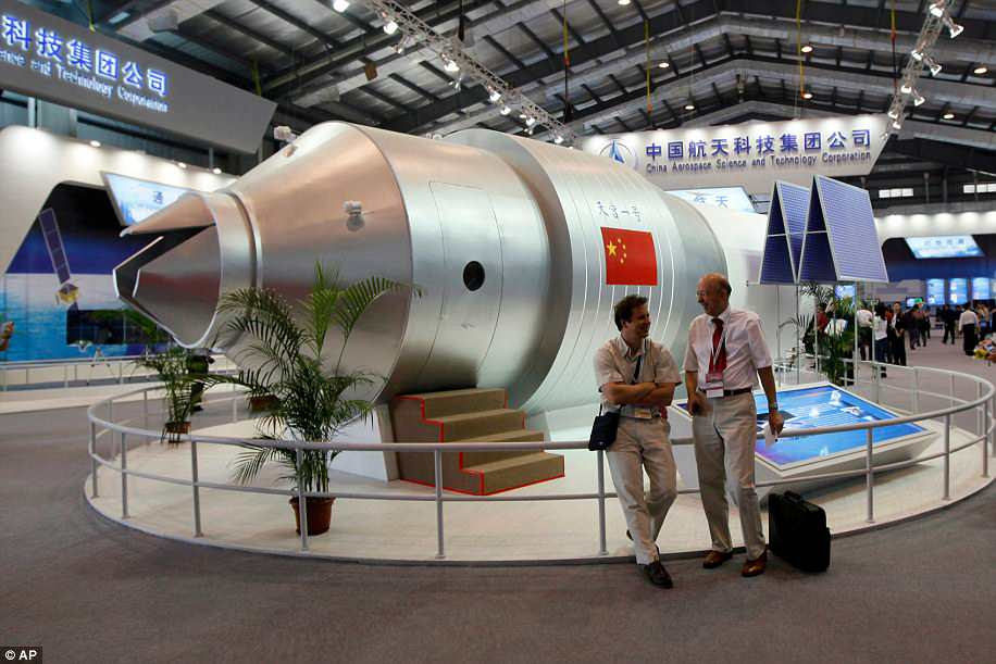 Visitors sit beside a model of China's Tiangong-1 space station in 2010. The station played host to two crewed missions and served as a test platform for perfecting docking procedures and other operations