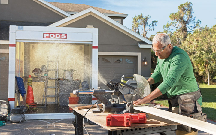 A contractor cutting wood for a pantry remodeling project with a PODS portable storage container in the background.