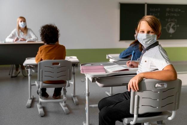 Children with medical masks learning in school with female teacher Free Photo