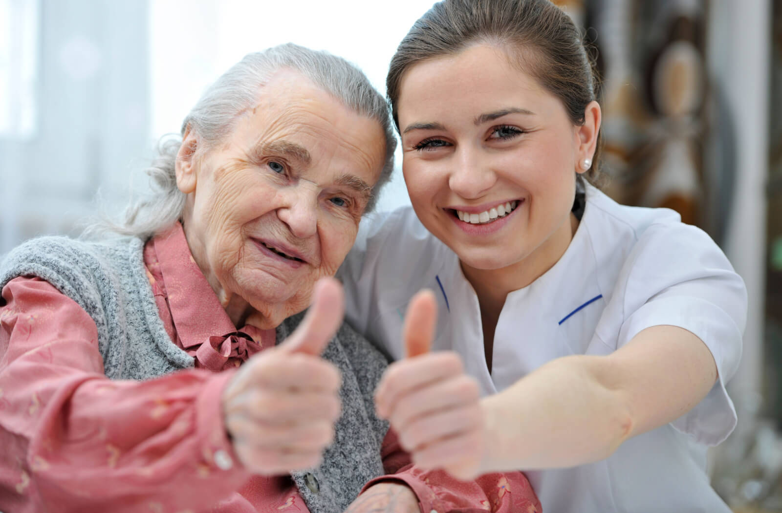 A senior woman and female nurse doing a thumbs up while smiling and looking directly at the camera.