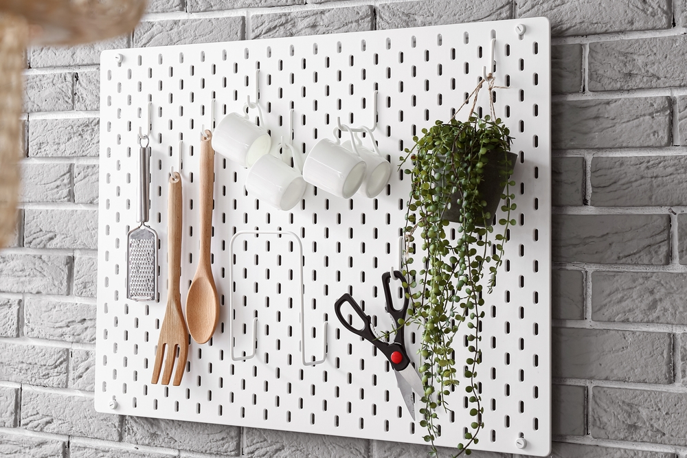 Pegboard organizer hanging on kitchen wall with utensils and plant.