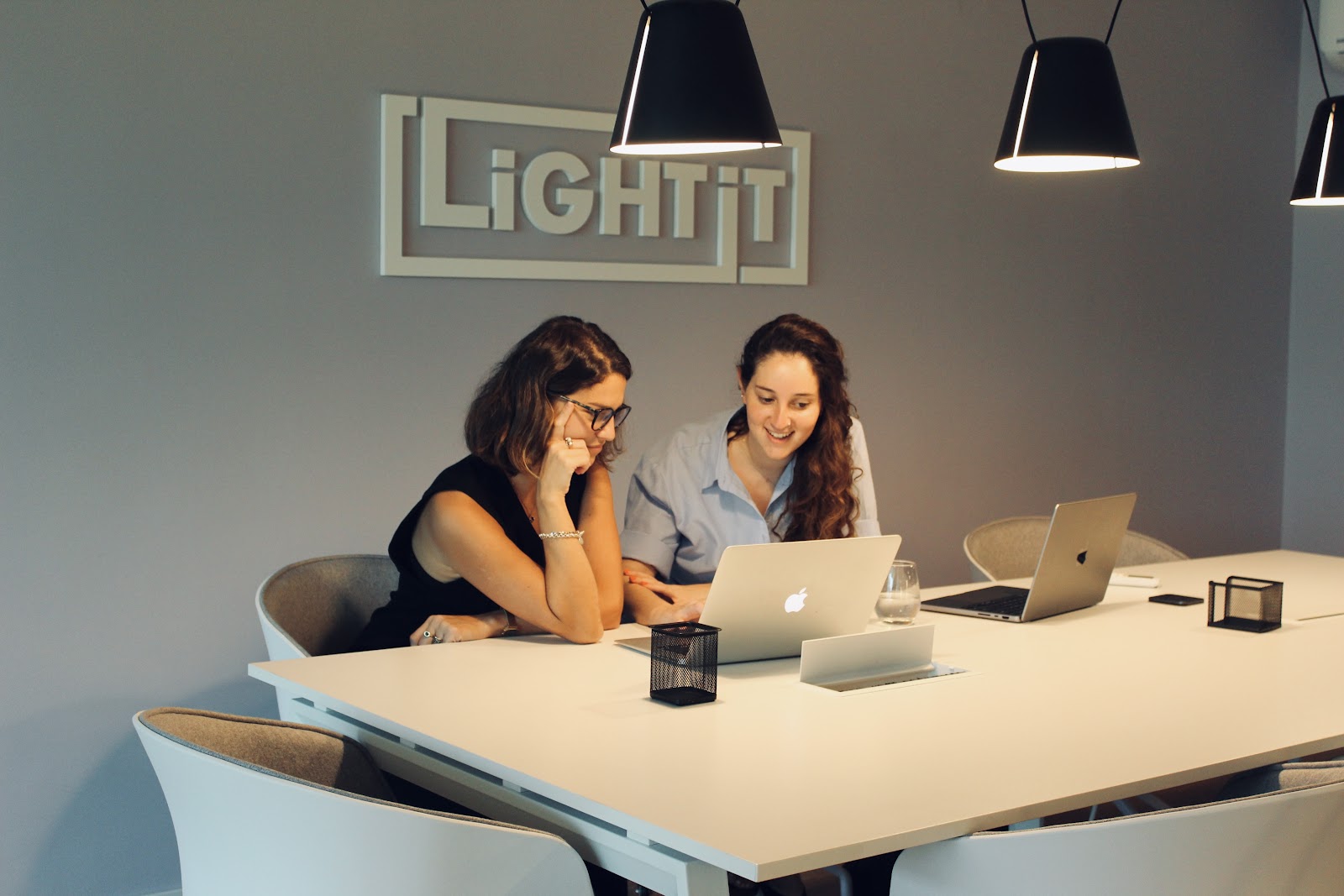 Two girls working together on her laptops in a conference room.