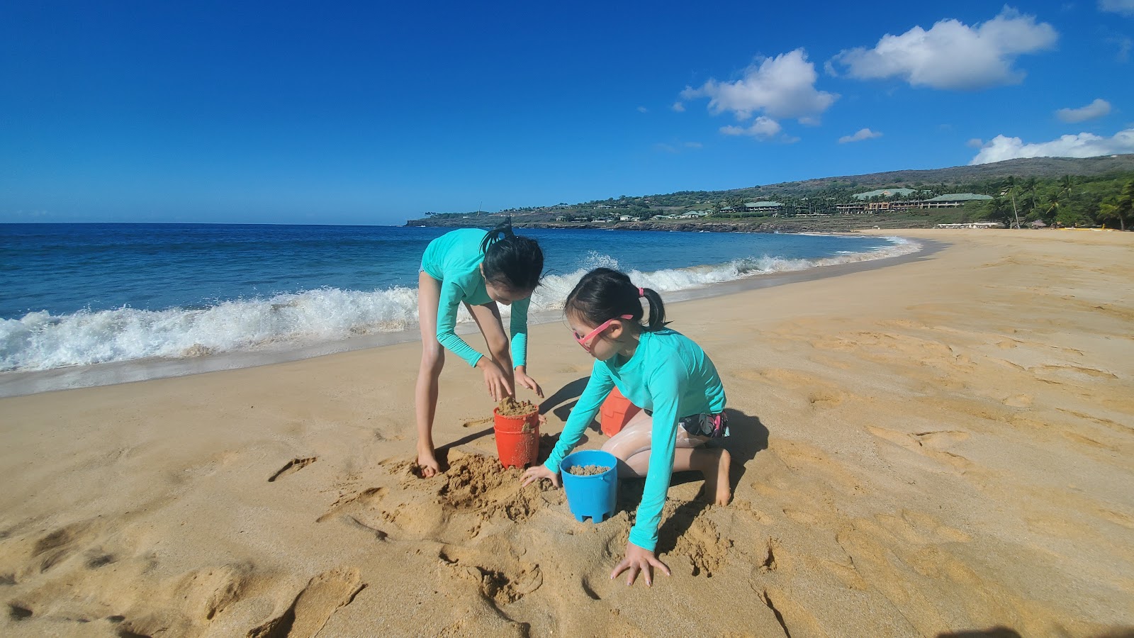 Image of two girls wearing teal rashguards playing on the beach in Lanai.