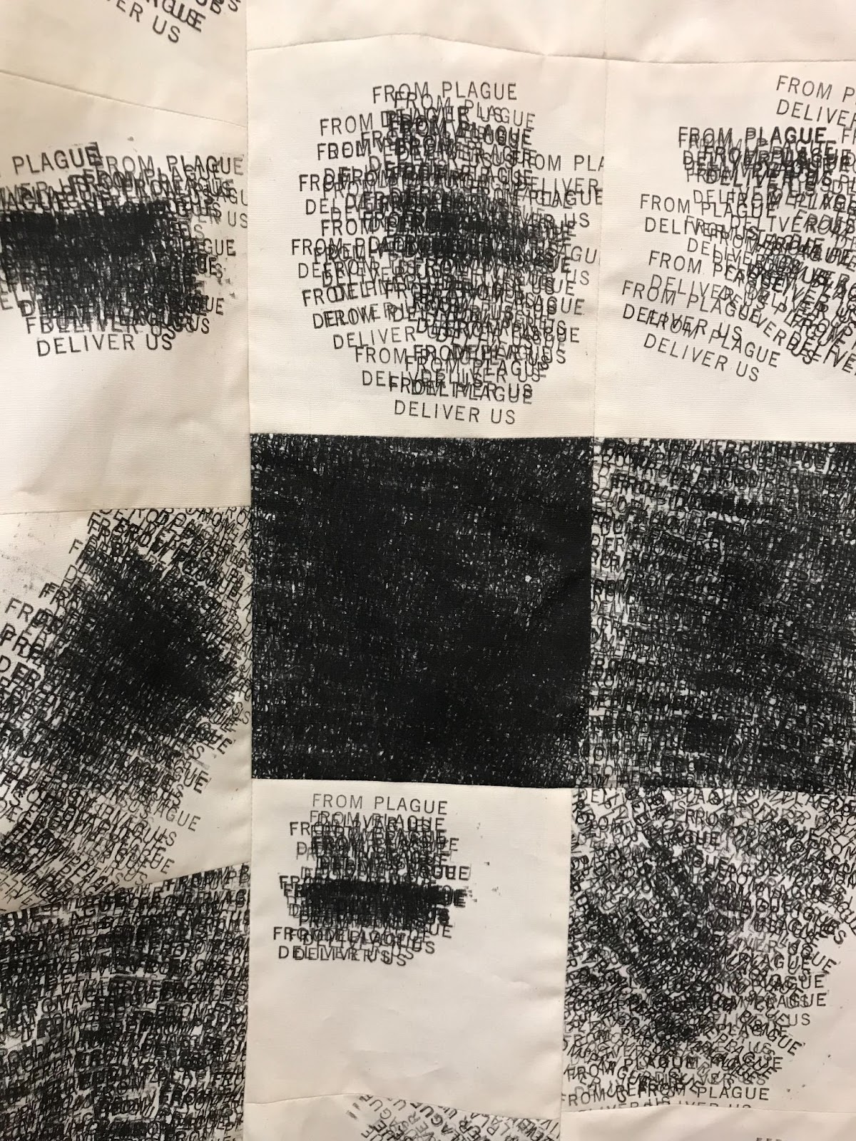 Detail image of a large textile documenting a year of new COVID-19 cases in Johnson county, Iowa. The textile is a cream color and higher case counts are indicated by clusters of overset text in black. The stamped message FROM PLAGUE DELIVER US can be distinguished in the clouds of text. Nine stamped squares measuring five by five inches are visible. 