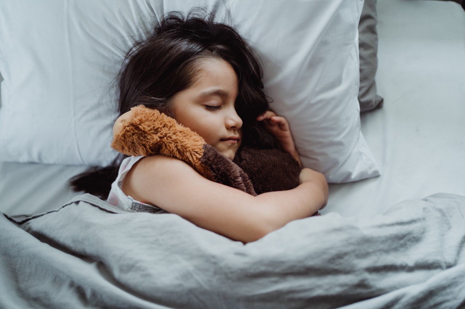 A young girl holds a teddy bear while sleeping in bed