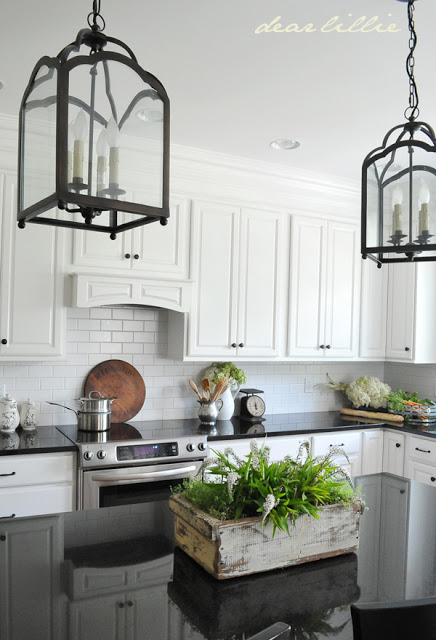 farmhouse black and white kitchen with white raised panel cabinets, glossy black countertops, black pendant lights and a white brick backsplash