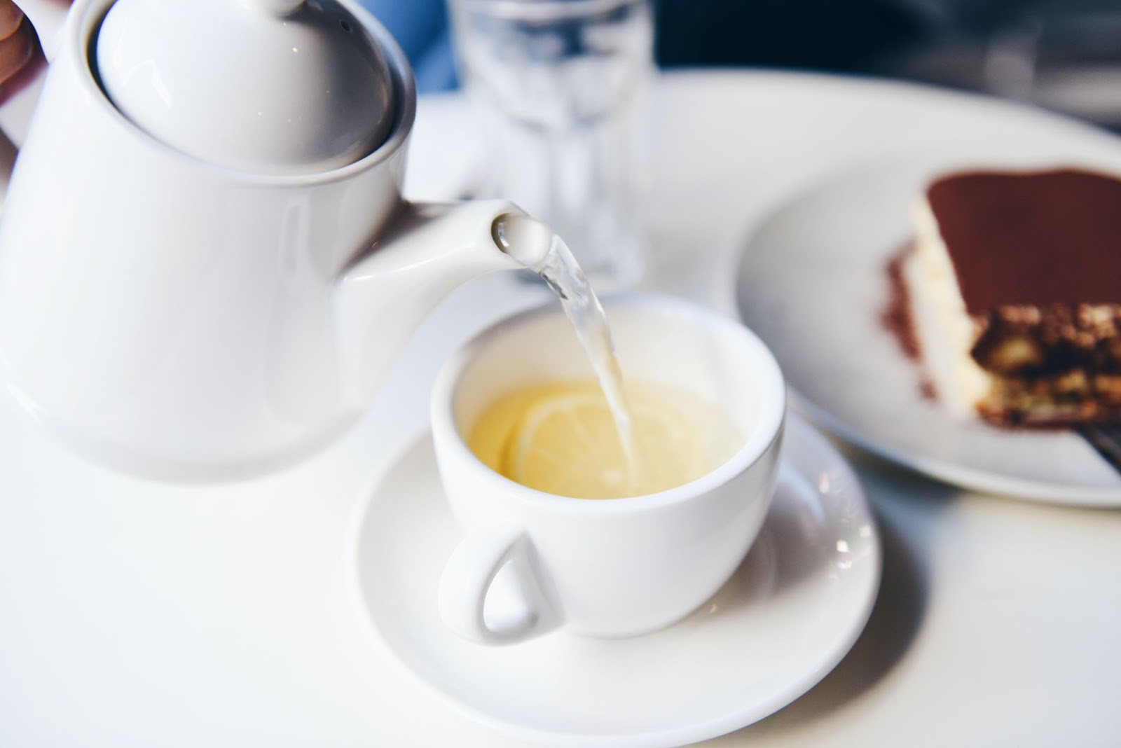 A white pot of tea being poured into a ceramic cup.