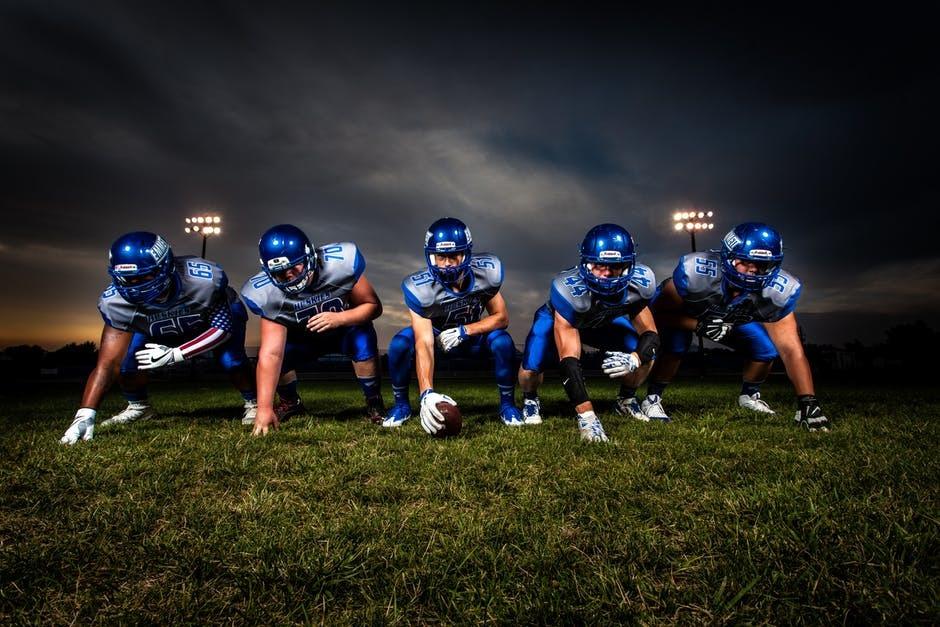 Football Players in Blue Jersey Lined Under Grey White Cloudy Sky during Sunset