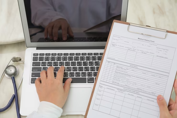 A top view of a doctor using a laptop and clipboard.