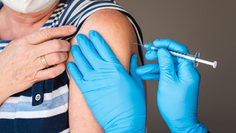 Close up of older woman getting injected with a vaccine in upper arm.